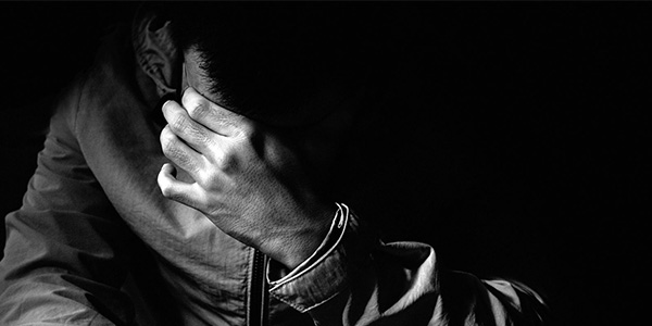 Black and white image of depressed looking man covering his face with his hand